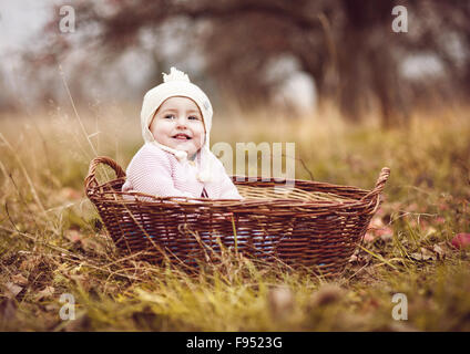 Felice bambina in vestiti caldi è seduta nel cestello in autunno la natura Foto Stock