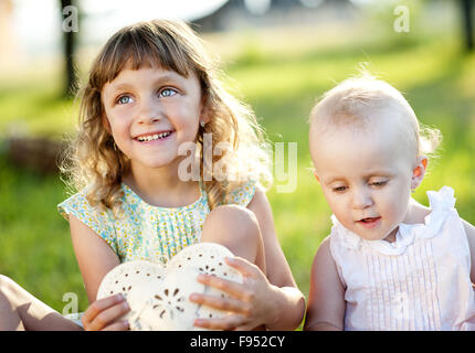 Due graziosi Piccole sorelle di ridere e giocare nel verde parco di sole Foto Stock