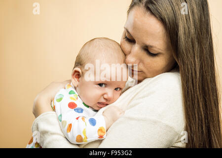 Il pianto del bambino con la madre studio shot su sfondo beige Foto Stock