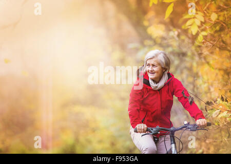 Attiva donna senior Bicicletta Equitazione in autunno la natura. Foto Stock