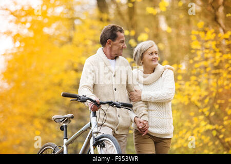 Seniors attivo avente a piedi con bici in autunno la natura. Essi avente tempo di romantica all'aperto. Foto Stock