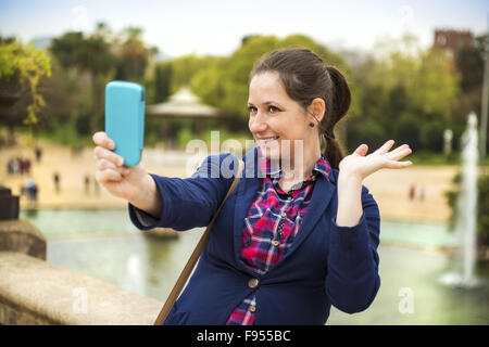 Piuttosto giovane turista femminile prendendo selfie di fronte alla fontana a Barcellona, Spagna. Foto Stock