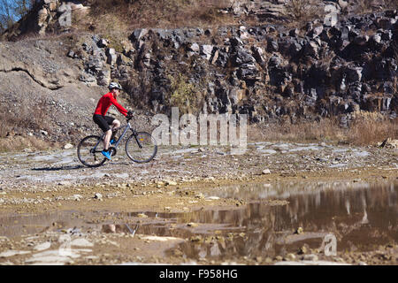 Ciclista uomo equitazione mountain bike lungo la pozza in cava Foto Stock