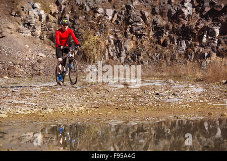 Ciclista uomo equitazione mountain bike lungo la pozza in cava Foto Stock