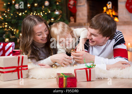 La famiglia felice con il piccolo figlio di avere un passatempo divertente nei pressi di albero di Natale e caminetto in soggiorno Foto Stock