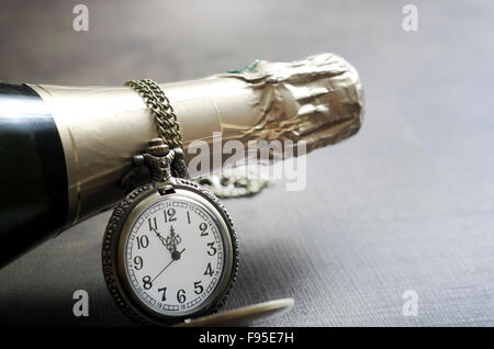 Dettaglio di un antico orologio da tasca con catena e champange collo di bottiglia con le mani dell'orologio si avvicina mezzanotte Foto Stock