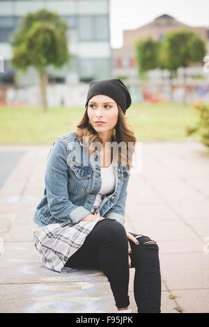 Giovane bella bionda caucasica capelli dritti donna seduta su una parete di piccole dimensioni che si affaccia a destra, pensieroso - riflessivo, pensando di future concept Foto Stock