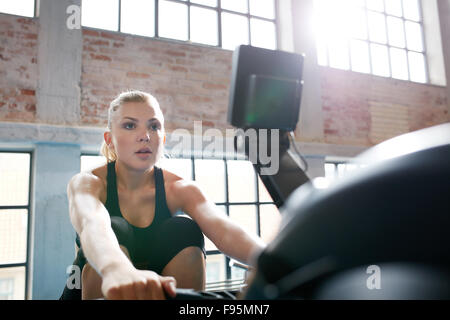 Montare la giovane donna che lavora fuori su un vogatore presso la palestra. Femmina caucasica facendo cardio esercizio nel fitness club. Foto Stock