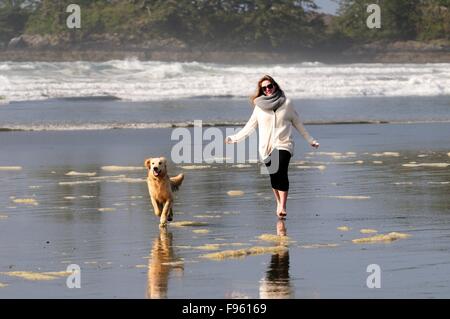 Una giovane donna e il suo cane (un Golden Retriever) eseguito con una sfera sulla spiaggia di Chesterman vicino a Tofino, BC. Foto Stock