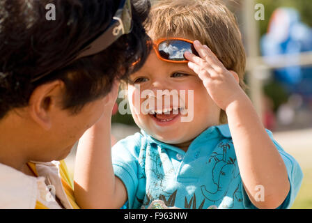 Un bimbo giggles con il suo papà come egli solleva gli occhiali da sole sopra la sua fronte. Foto Stock