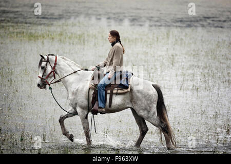 Una ragazza cavalca un cavallo bianco in acqua a Capilla vieja, Estado de Mexico, Messico. (Sfocatura) Foto Stock