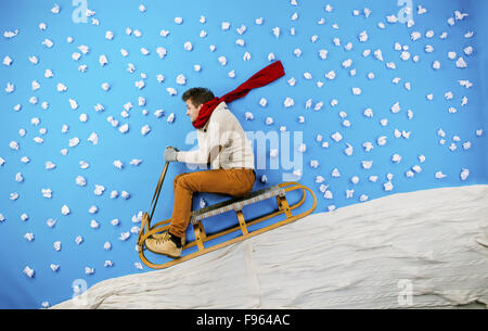 Felice giovane uomo sulla slitta avendo divertimento contro lo sfondo blu con i fiocchi di neve Foto Stock