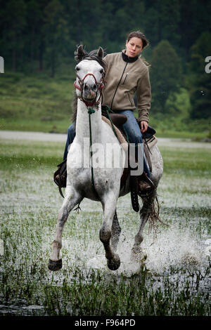 Una ragazza cavalca un cavallo bianco in acqua a Capilla vieja, Estado de Mexico, Messico. (Sfocatura) Foto Stock
