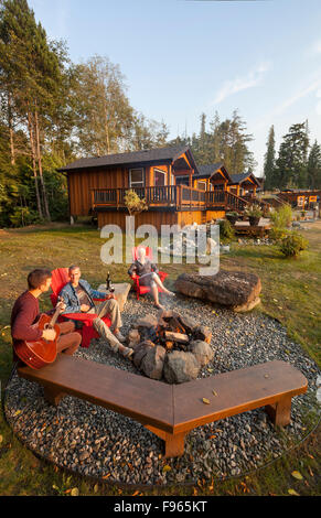 Gli amici si radunano attorno a un fuoco mentre soggiornate presso il Ecoscape cabine stabilimento situato a Port Hardy Foto Stock