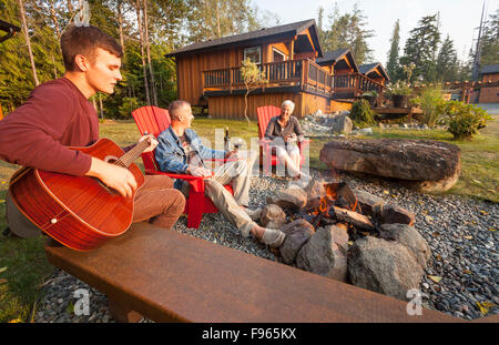 Gli amici si radunano attorno a un fuoco mentre soggiornate presso il Ecoscape cabine stabilimento situato a Port Hardy Foto Stock