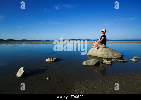 Una donna matura si rilassa tra rocce a bassa marea mentre visitano Sidney Spit. Il Gulf Islands National Park riserva, Vancouver Foto Stock