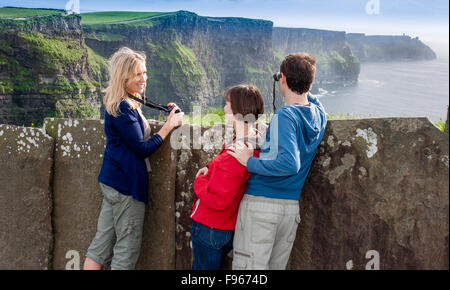 I giovani adulti in vacanza prendendo fotografie. Scogliere di Moher, Irlanda Foto Stock