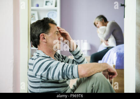 Donna matura siiting sul letto è la paura di un uomo. La donna è vittima di violenza domestica e abusi. Foto Stock