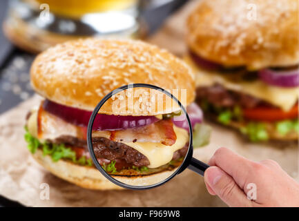 Lente di ingrandimento esaminando burger Foto Stock