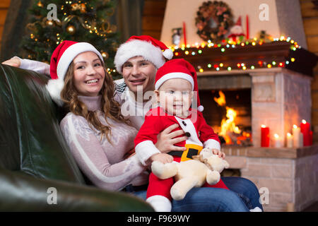 La famiglia felice con il bambino seduto sul divano un divertimento vicino a albero di Natale e caminetto in soggiorno Foto Stock