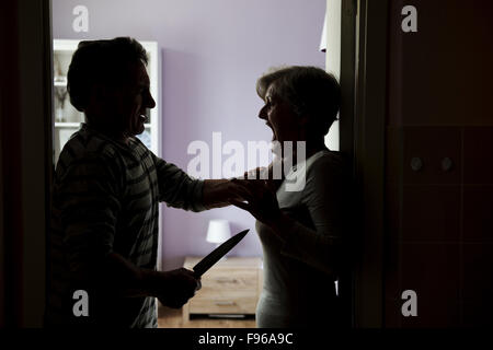 Silhouette di Coppia matura lotta, l'uomo è di attaccare la donna con il coltello. La donna è vittima di violenza domestica Foto Stock