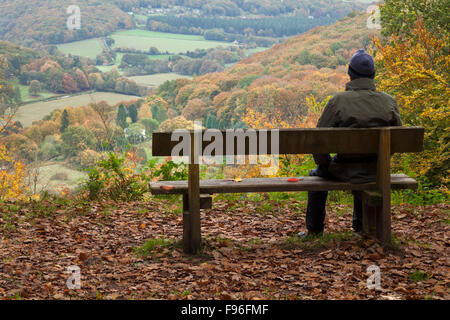 Un maschio maturo in outdoor gear seduto su una panca in legno che si affaccia sulla valle del Wye in autunno nei pressi di Llandogo, Momouthshire, Wales, Regno Unito Foto Stock