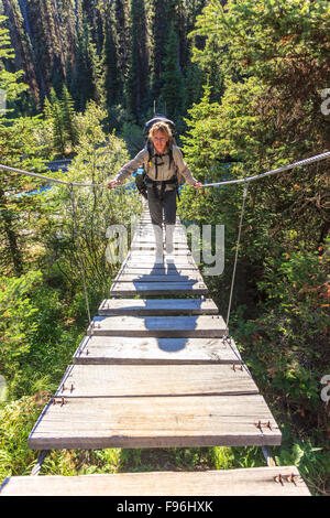 Un packer indietro attraversa una sospensione ponte su un fiume di Kootenay National Park, British Columbia, Canada. Modello rilasciato Foto Stock