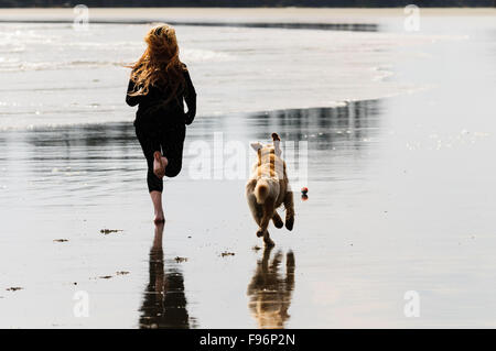 Una giovane donna e il suo Golden Retriever acceso dopo una palla mentre sulla spiaggia di Chesterman in Tofino, British Columbia. Foto Stock