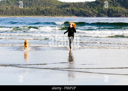 Una giovane donna in esecuzione con il suo Golden Retriever Chesterman sulla spiaggia vicino a Tofino British Columbia. Foto Stock