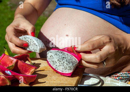 Donna incinta di mangiare la frutta del drago, preparazione, ventre in gravidanza Foto Stock