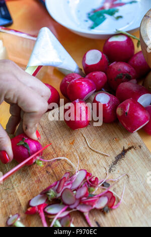 Donna che taglia i raggi con un coltello su un tavolo di legno in cucina Foto Stock