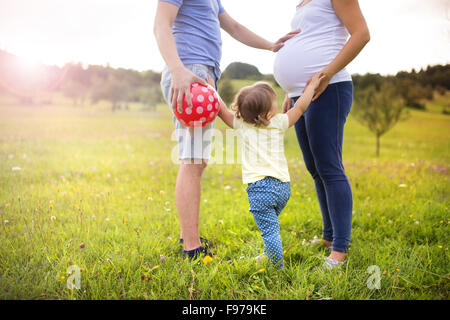 Gravidanza felice famiglia con bambina divertendosi con sfera in estate la natura Foto Stock