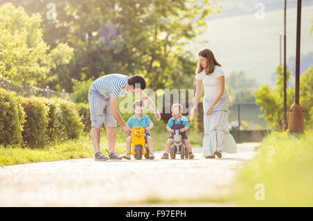 La famiglia felice con poco figli sulla moto nel verde parco di sole Foto Stock