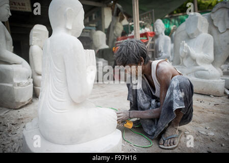 MANDALAY, Myanmar - gli artigiani locali intraprendono il lavoro polveroso e sfrenato di intagliare statue del Buddha in marmo. Poiché il buddismo è la religione dominante in Myanmar, c'è una notevole domanda di statue, con i clienti in grado di scegliere tra una miriade di pose, dimensioni e stili. Gli artigiani sono raggruppati in una strada nel quartiere Chanmyathazi di Mandalay vicino alla Pagoda Mahamuni. Foto Stock