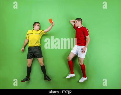 Arbitro dando cartellino rosso ad un giocatore di calcio. Studio shot su sfondo verde. Foto Stock