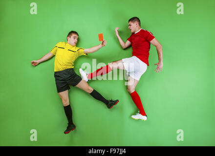 Arbitro dando cartellino rosso ad un giocatore di calcio. Studio shot su sfondo verde. Foto Stock