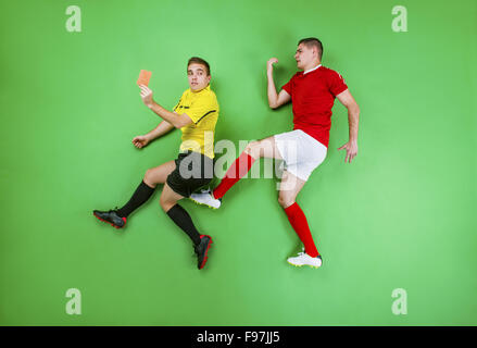 Arbitro dando cartellino rosso ad un giocatore di calcio. Studio shot su sfondo verde. Foto Stock