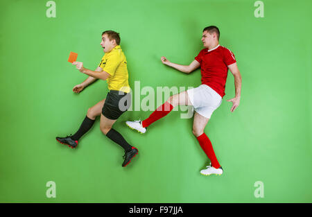 Arbitro dando cartellino rosso ad un giocatore di calcio. Studio shot su sfondo verde. Foto Stock