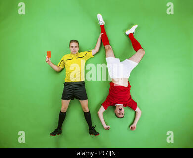 Arbitro dando cartellino rosso ad un giocatore di calcio. Studio shot su sfondo verde. Foto Stock