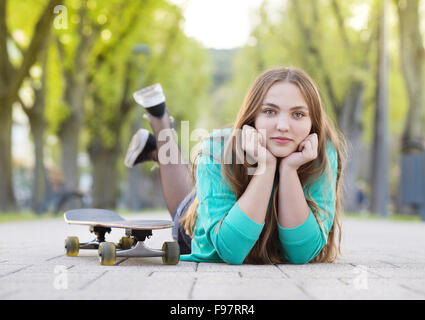 Ritratto di bella ragazza adolescente con lo skateboard giacente sulla pavimentazione in vicolo verde Foto Stock