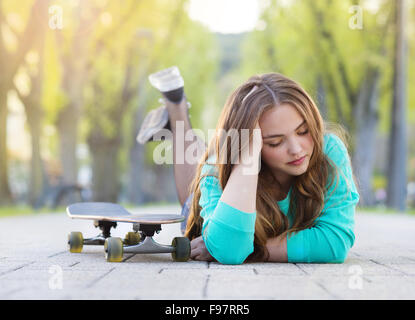 Ritratto di bella ragazza adolescente con lo skateboard giacente sulla pavimentazione in vicolo verde Foto Stock