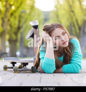 Ritratto di bella ragazza adolescente con lo skateboard giacente sulla pavimentazione in vicolo verde Foto Stock