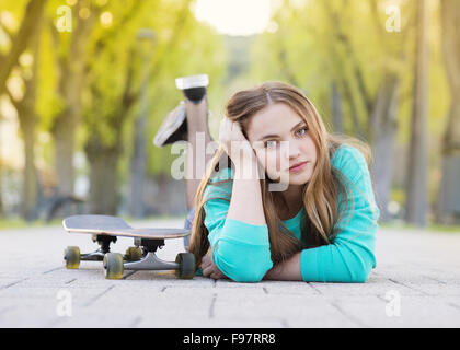 Ritratto di bella ragazza adolescente con lo skateboard giacente sulla pavimentazione in vicolo verde Foto Stock