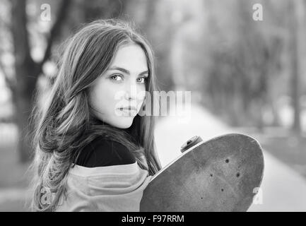 Bianco e nero ritratto della bella ragazza adolescente con lo skateboard in parco verde Foto Stock