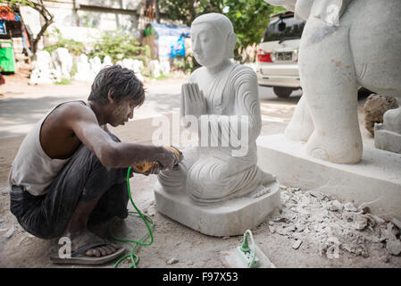 MANDALAY, Myanmar - gli artigiani locali intraprendono il lavoro polveroso e sfrenato di intagliare statue del Buddha in marmo. Poiché il buddismo è la religione dominante in Myanmar, c'è una notevole domanda di statue, con i clienti in grado di scegliere tra una miriade di pose, dimensioni e stili. Gli artigiani sono raggruppati in una strada nel quartiere Chanmyathazi di Mandalay vicino alla Pagoda Mahamuni. Foto Stock