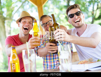 Tre amici felici di bere birra, chattare e divertirsi in pub garden Foto Stock