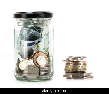 Vaso di vetro con delle monete e delle banconote provenienti da tutto il mondo su uno sfondo bianco - concetto di risparmio Foto Stock