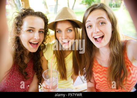 Tre belle ragazze bere e tenendo selfie con lo smartphone in pub garden Foto Stock