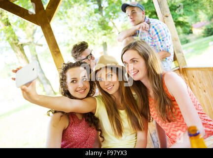 Tre belle ragazze bere e tenendo selfie con lo smartphone in pub garden Foto Stock