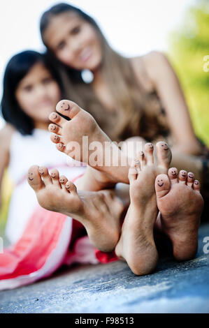 Due sorelle di ridere e abbracciando sul marciapiede nel verde parco di sole Foto Stock